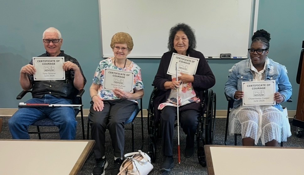 4 adults sit side by side holding certificates of courage